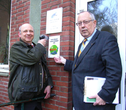 Bezirksamtsleiter Torsten Meinberg (links) und Rolf de Vries beim Anbringen des NUE-Schildes (Foto Gisela Baudy)
