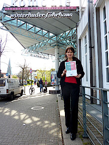Gisela Baudy mit Urkunde und Elbbrücken-Plakat vor der Komödie des Winterhuder Fährhauses. (Foto Chris Baudy)